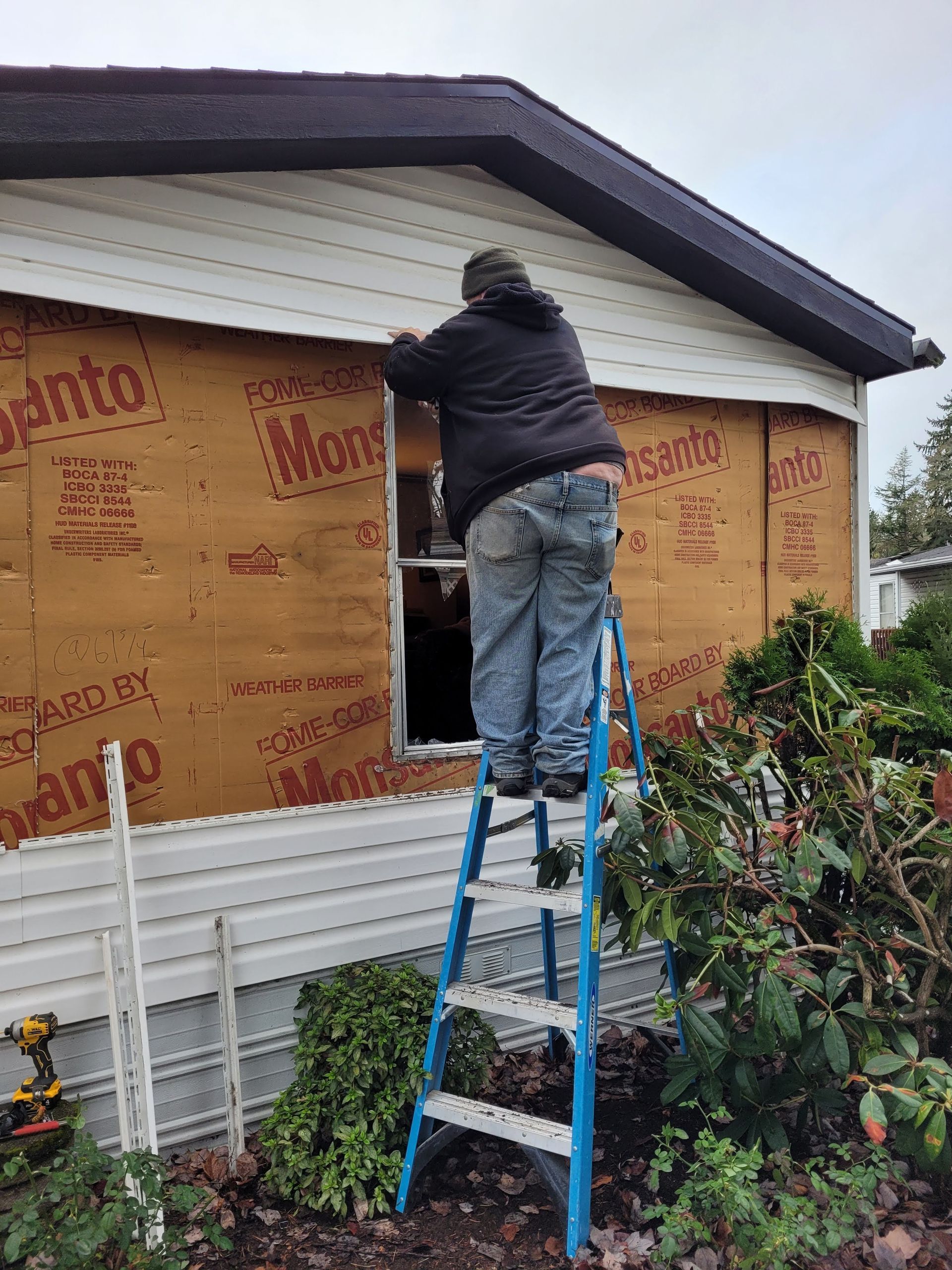 A man is standing on a ladder fixing a window on the side of a house.