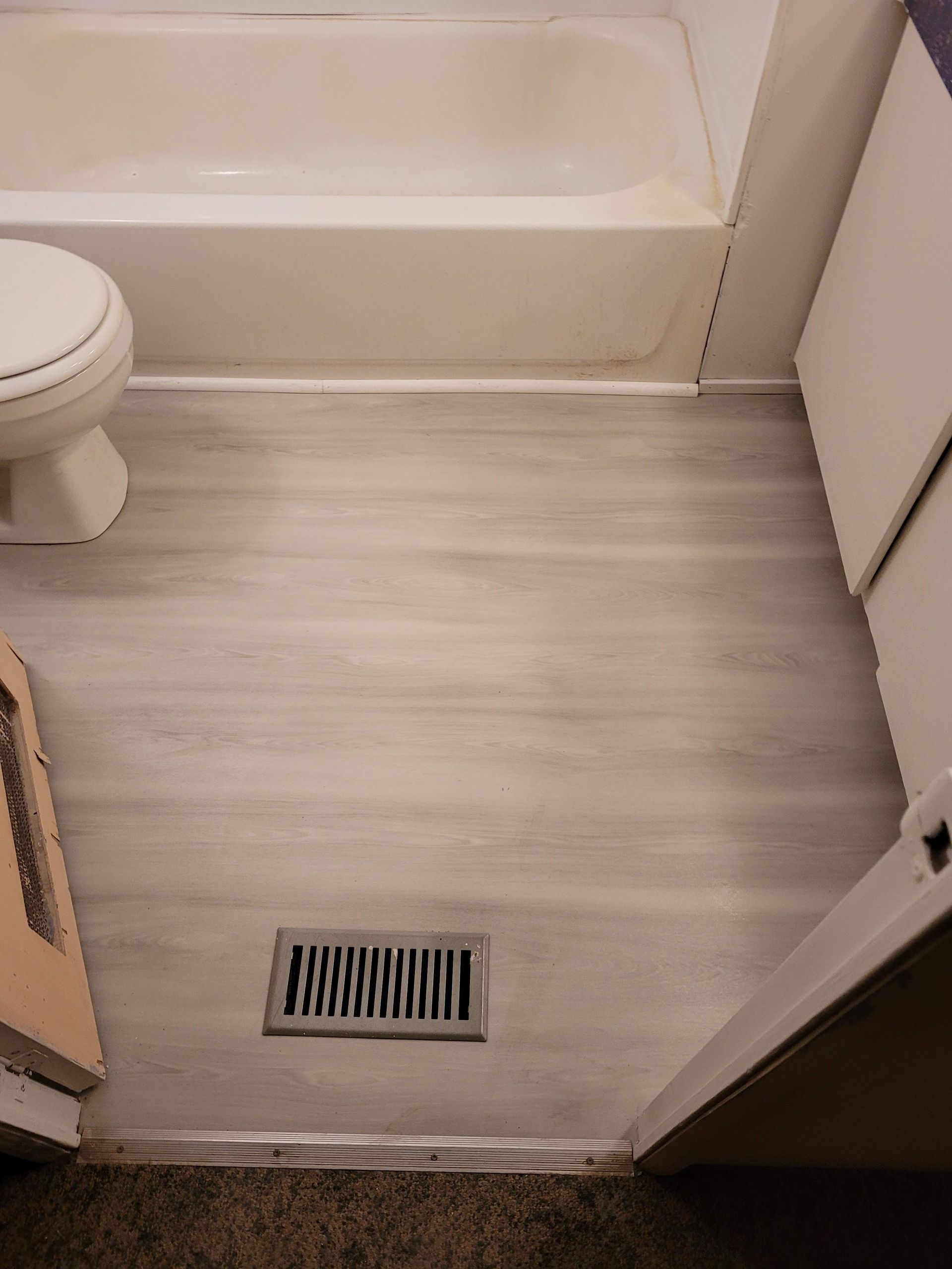 A bathroom with a toilet , bathtub and air vent.