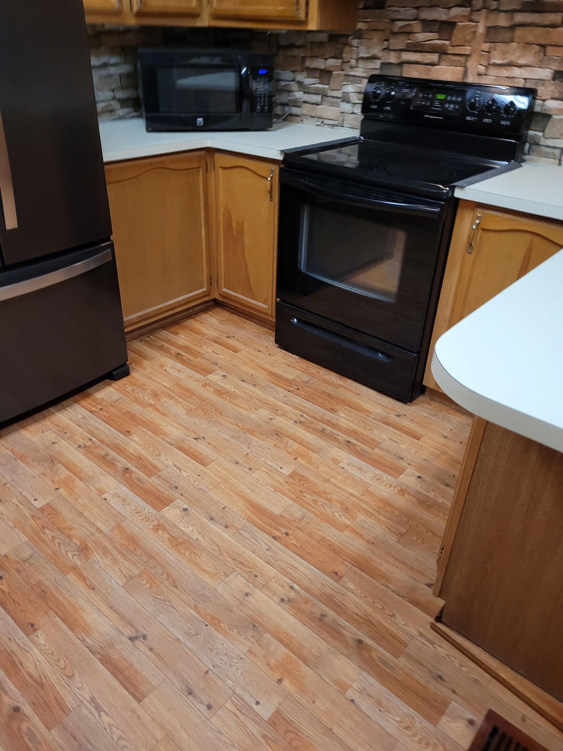 A kitchen with a stove , refrigerator , microwave and wooden floors.