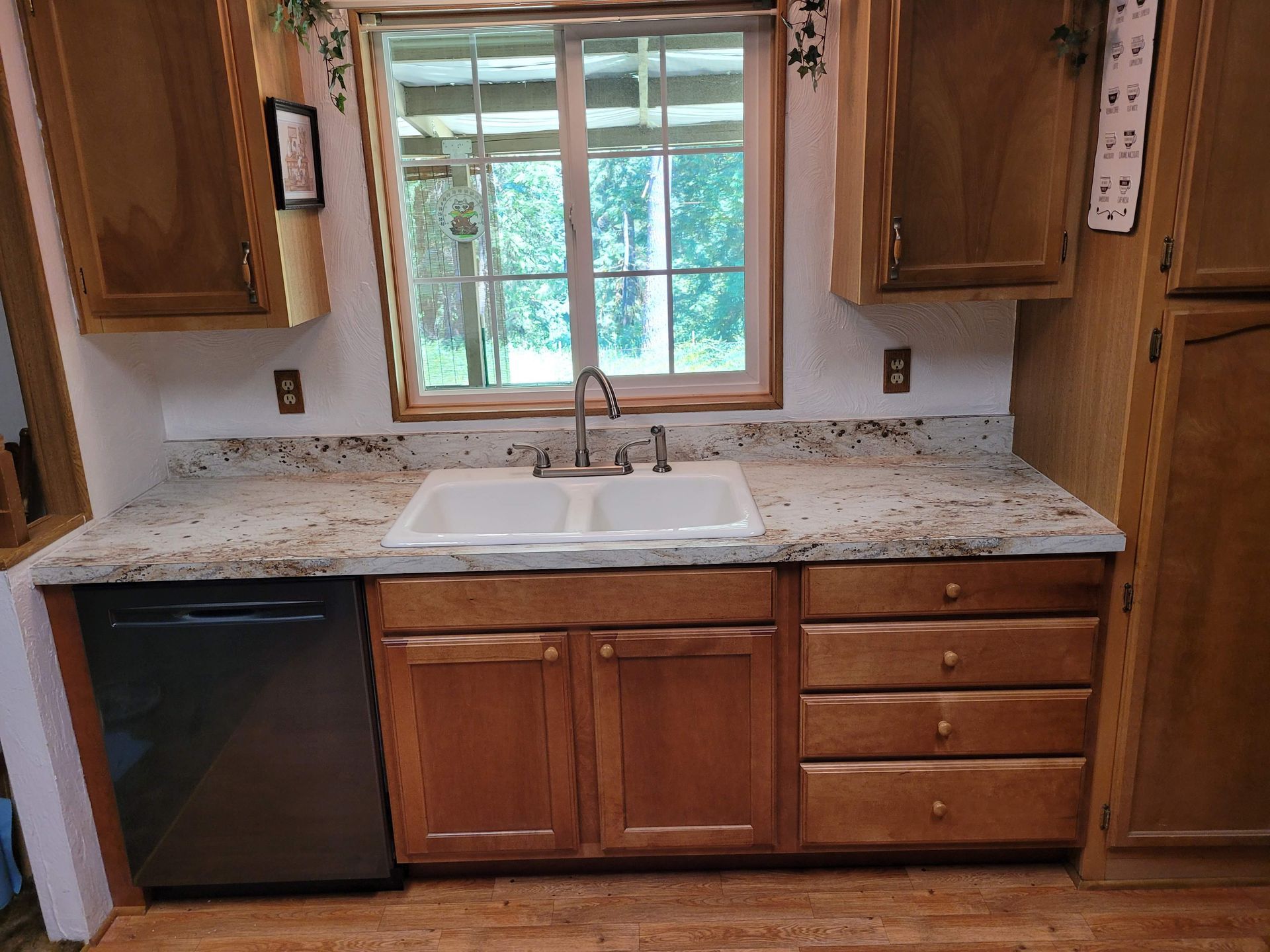 A kitchen with wooden cabinets , a sink , a dishwasher , and a window.