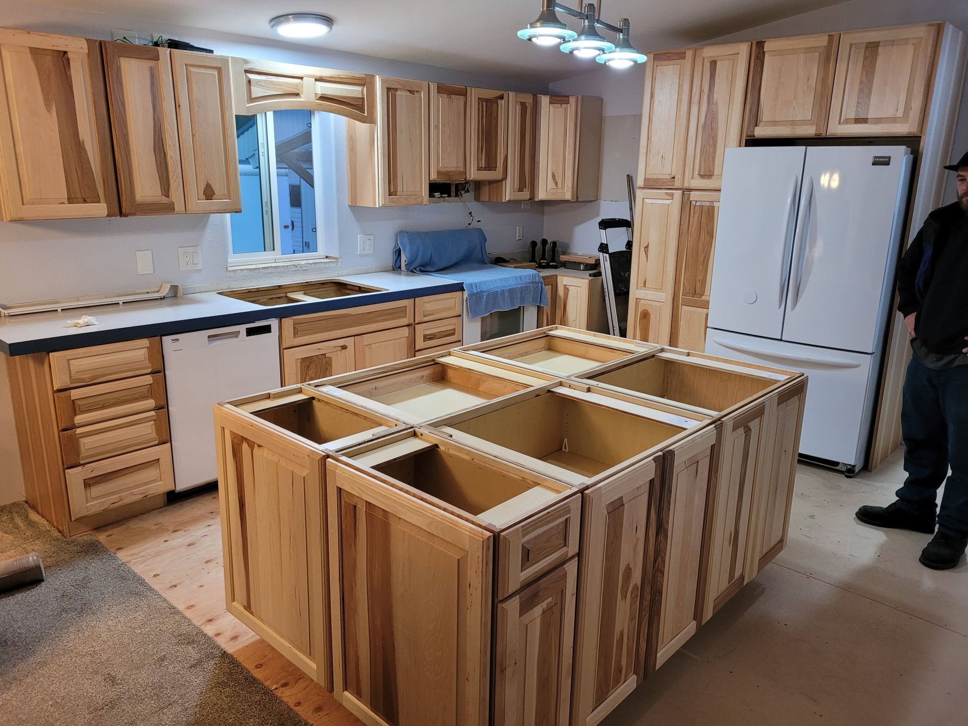 A man is standing in a kitchen with wooden cabinets and a refrigerator.