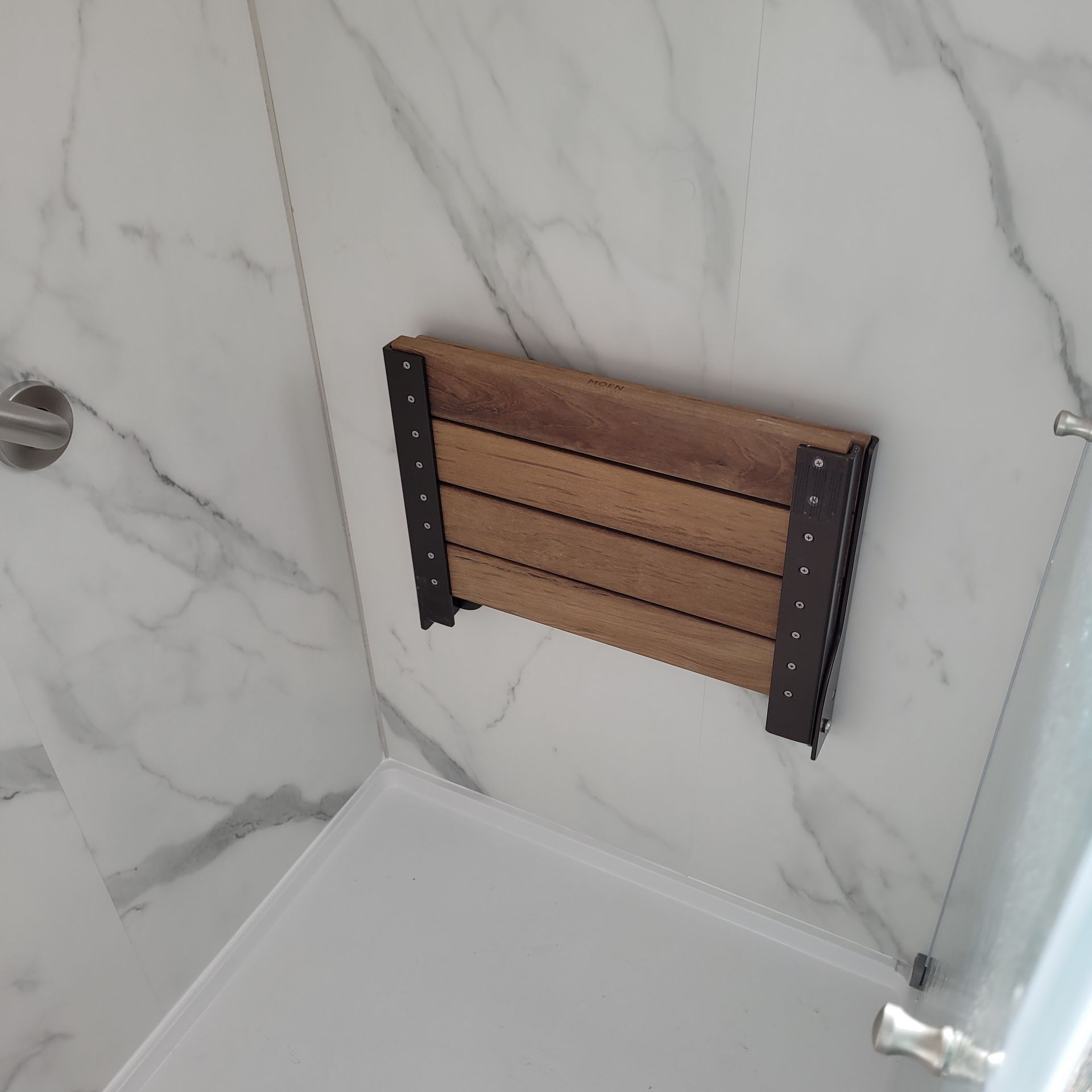 A wooden shower seat is attached to a marble wall