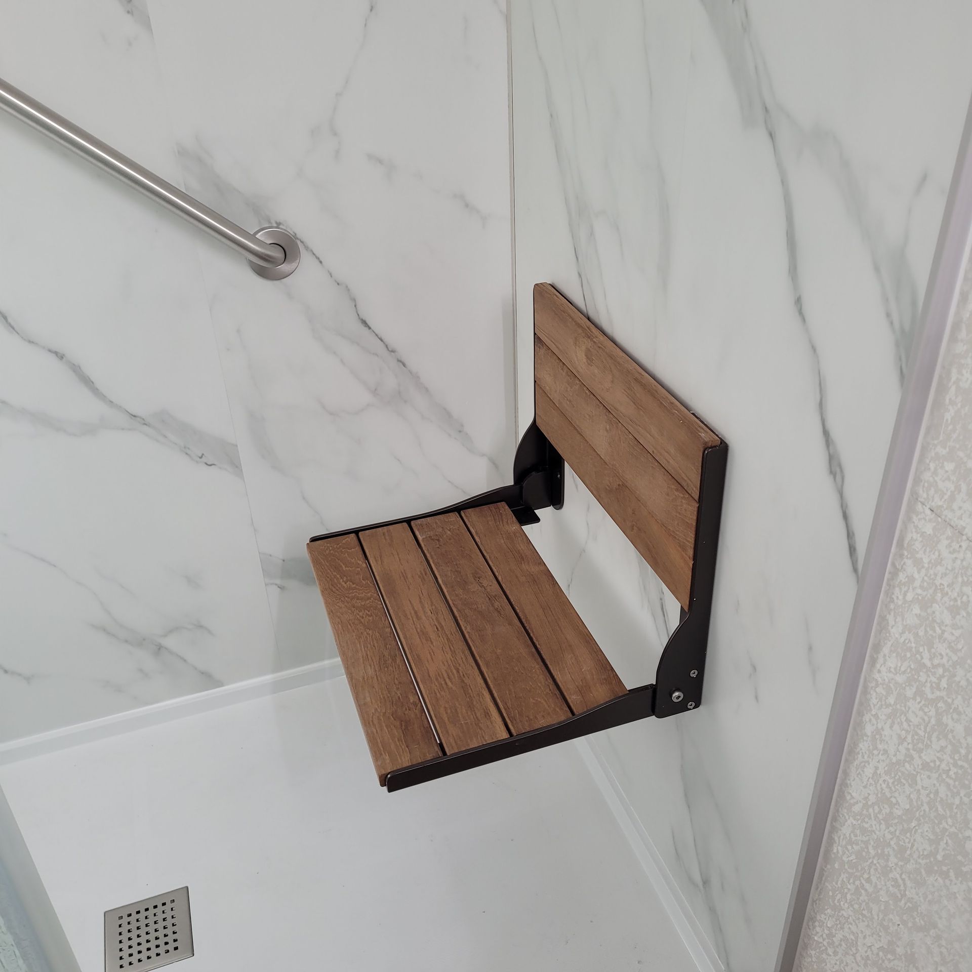 A shower with a wooden seat and a stainless steel railing