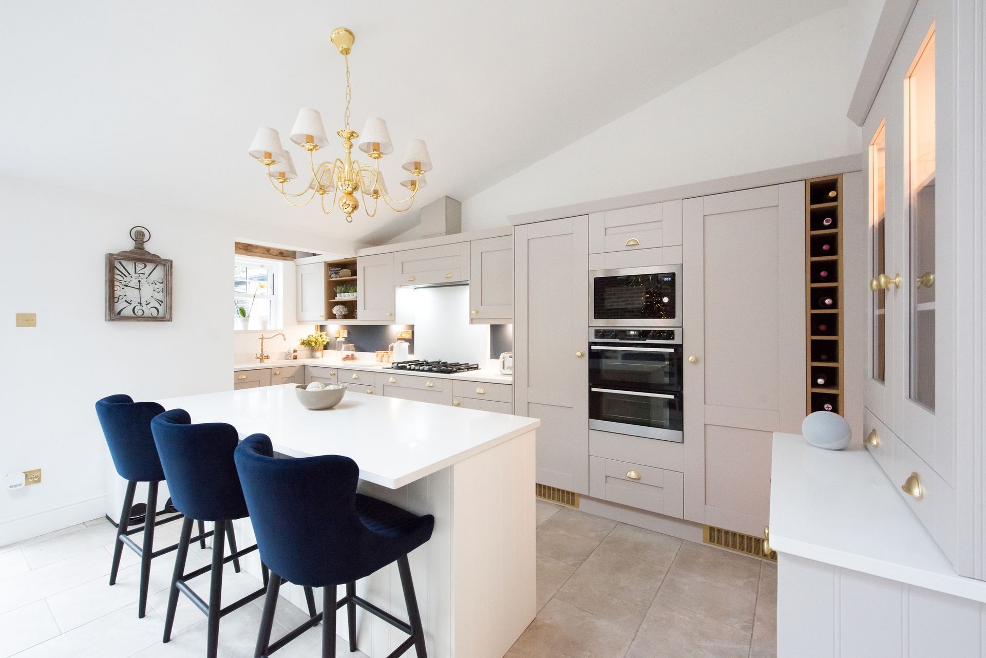 A kitchen with white cabinets and blue chairs and a clock on the wall.