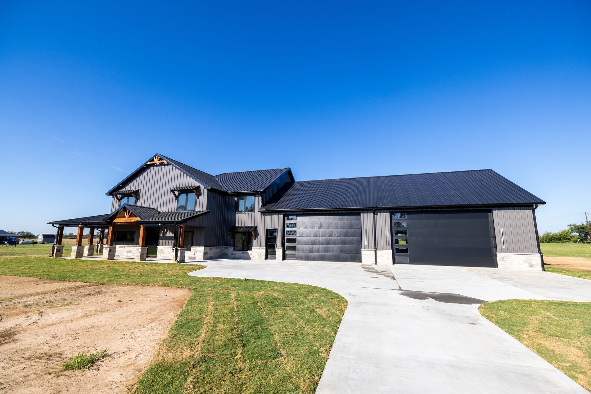 A large house with a black garage door is sitting on top of a lush green field.