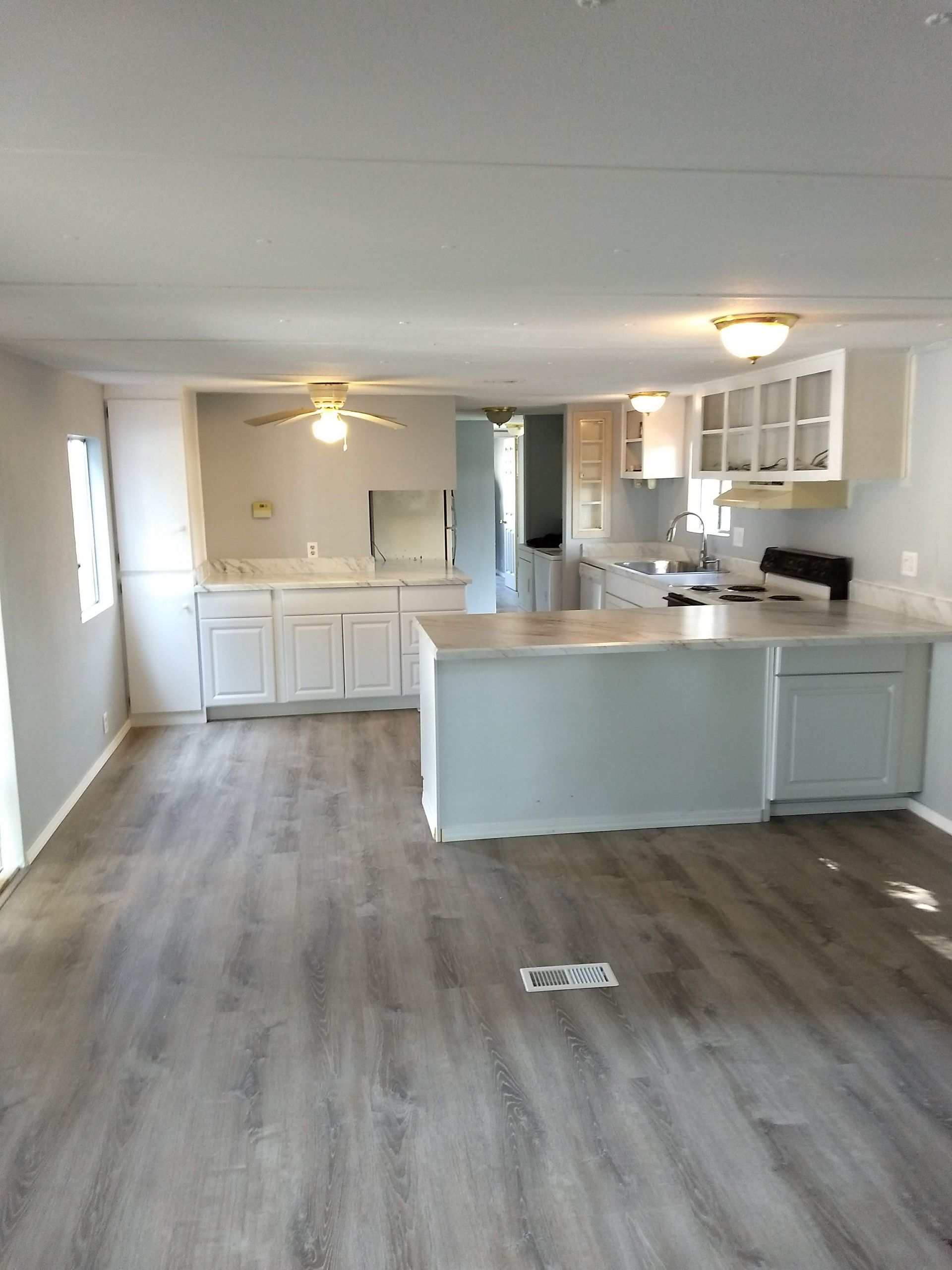 An empty kitchen with white cabinets and a wooden floor.