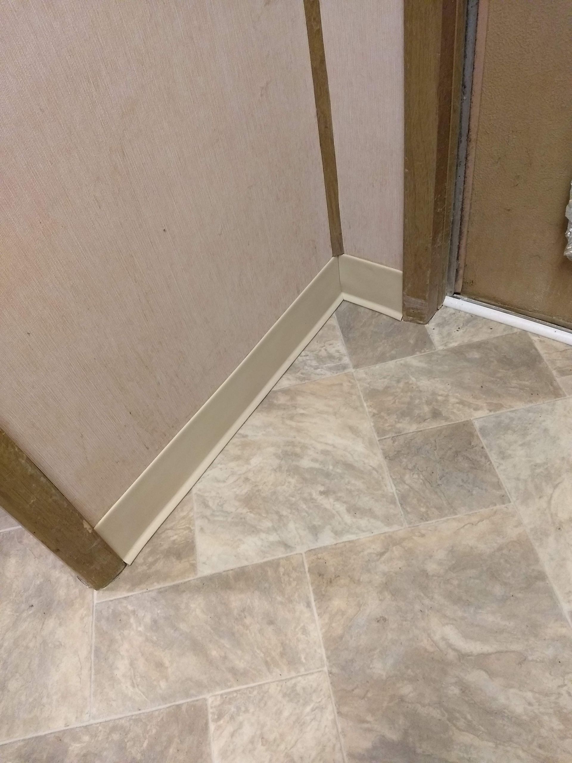 A corner of a room with a tile floor and a door.