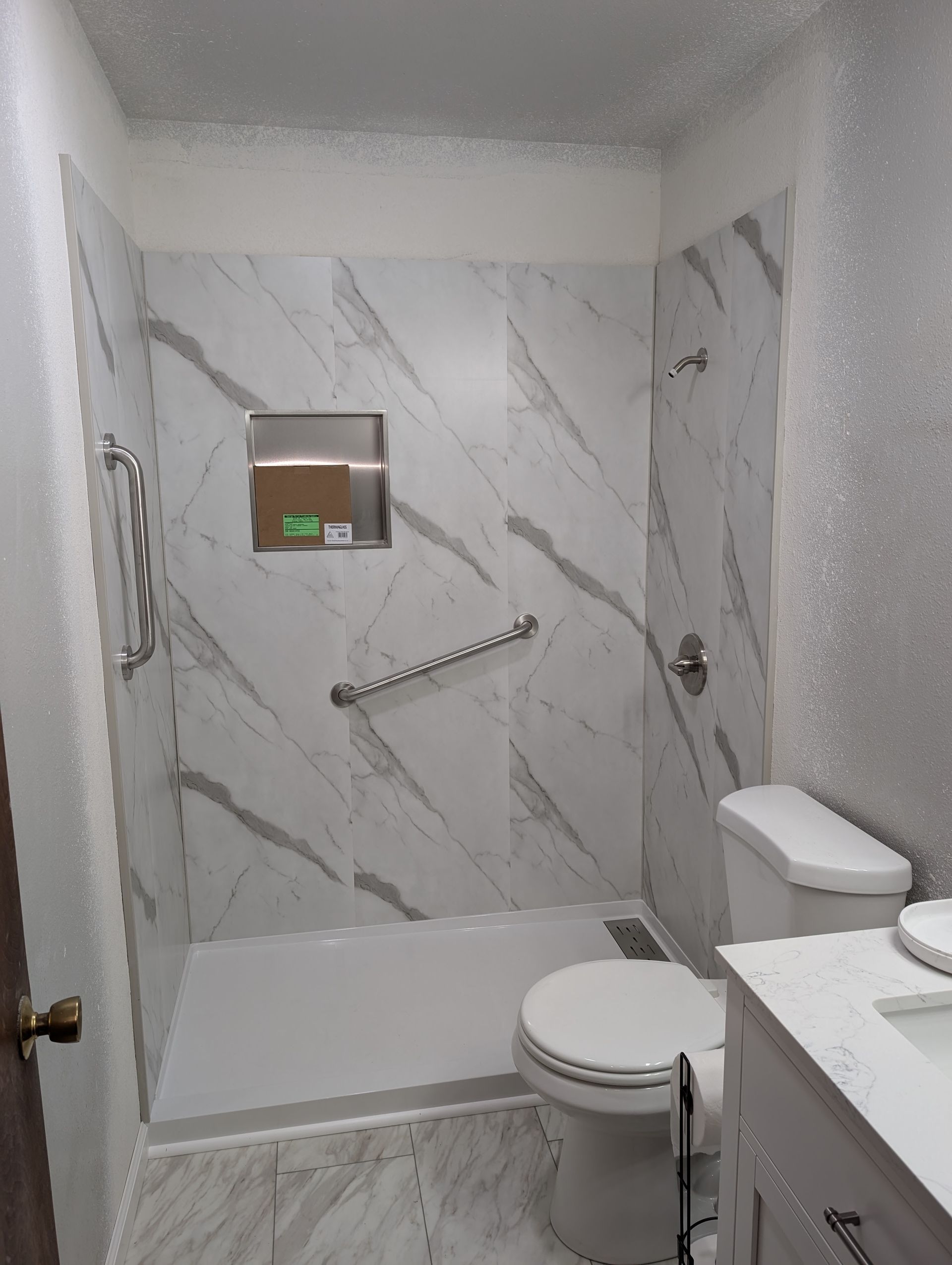 A bathroom with a toilet , sink , shower and marble walls.