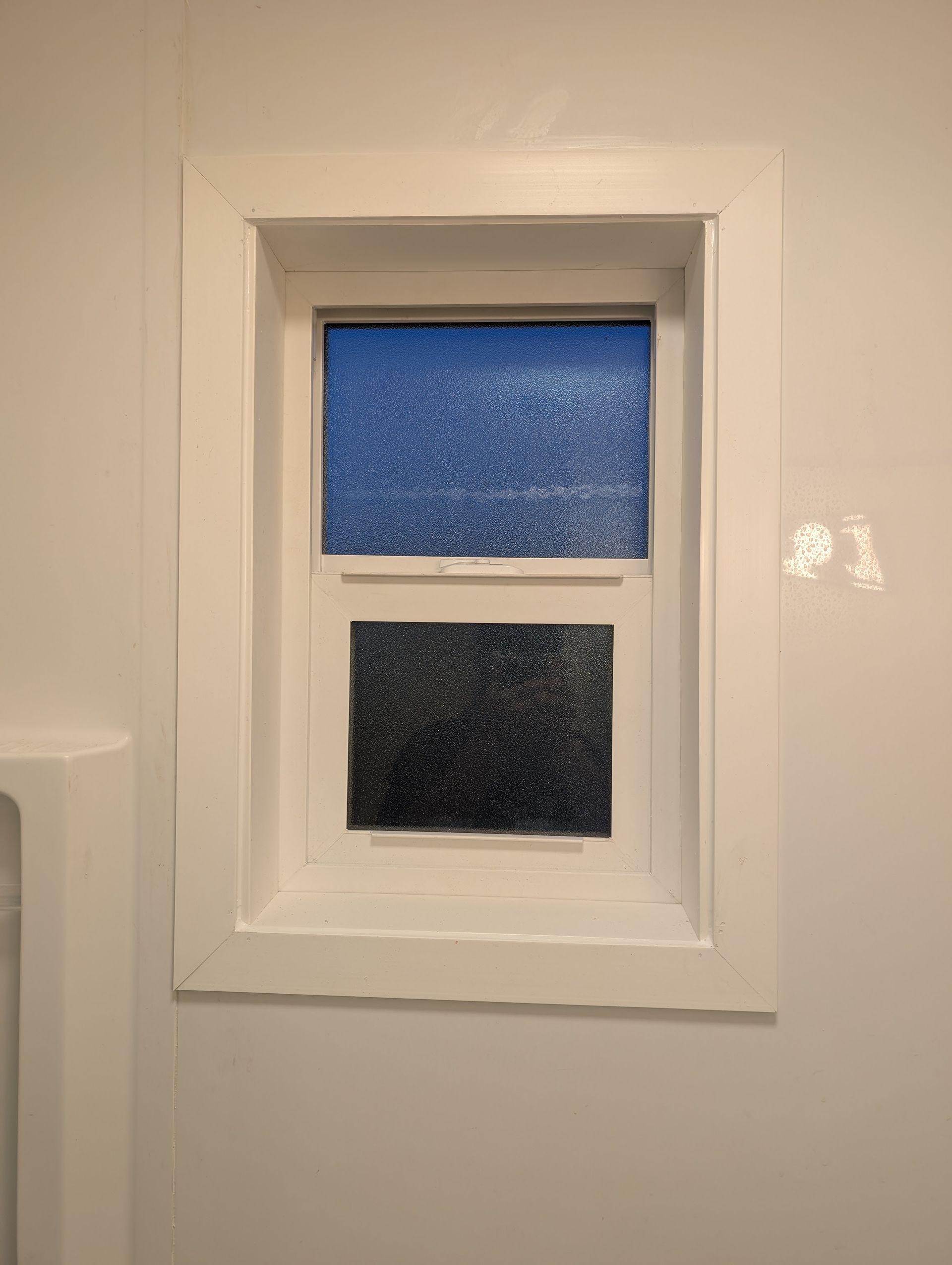 A bathroom window with a white frame and a blue glass window.