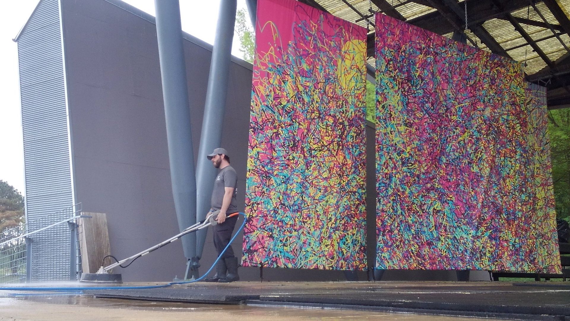 A man is standing in front of a colorful wall holding a hose.