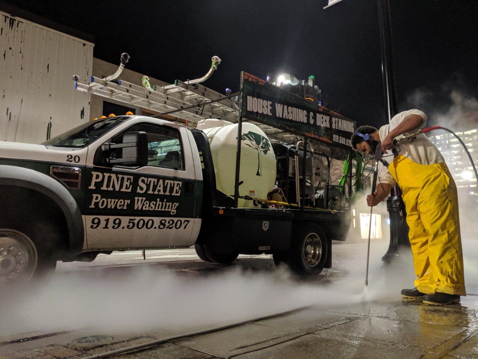 A man in yellow overalls is standing next to a pine state power washing truck.