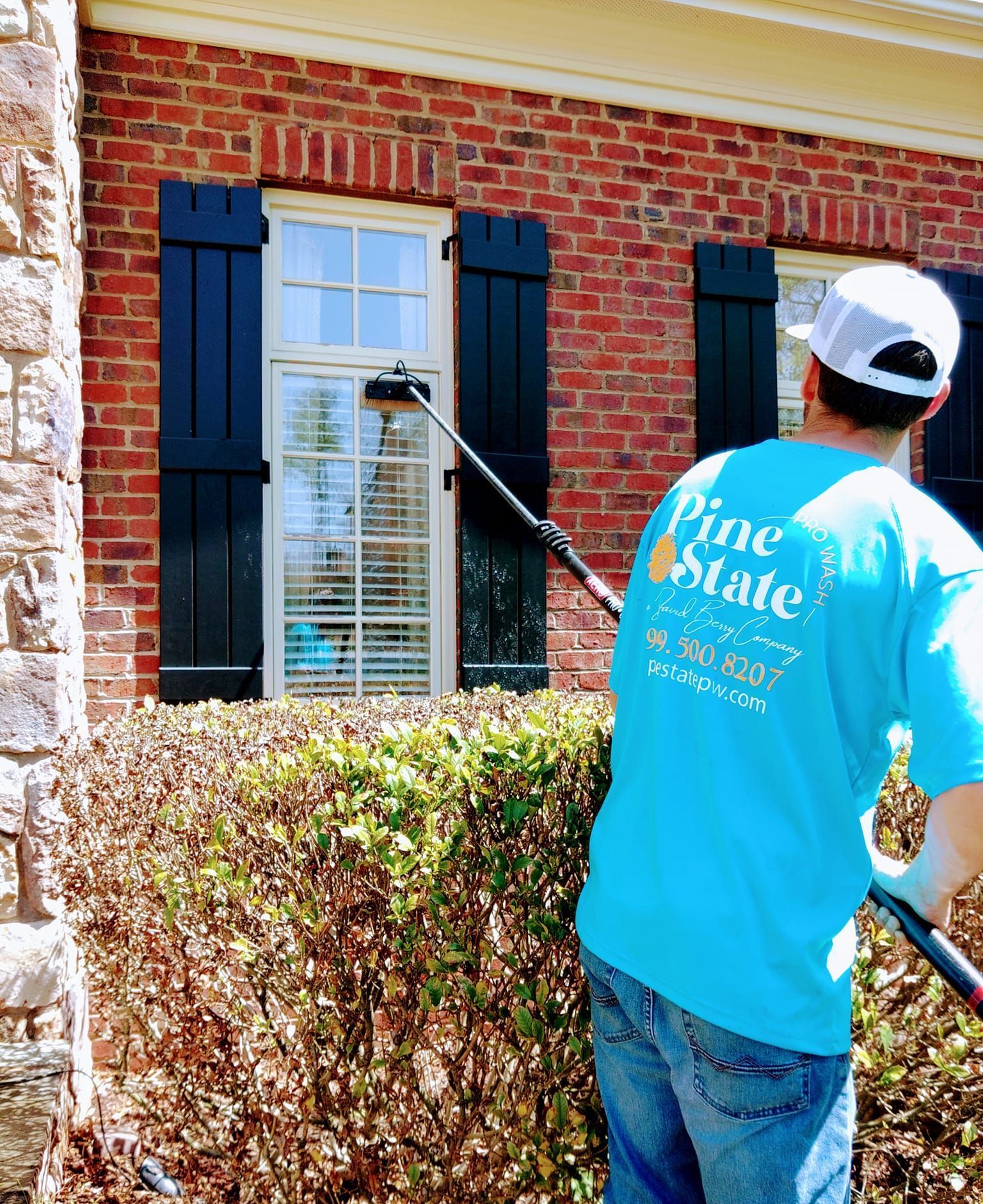 A man in a pine state shirt is cleaning a window.