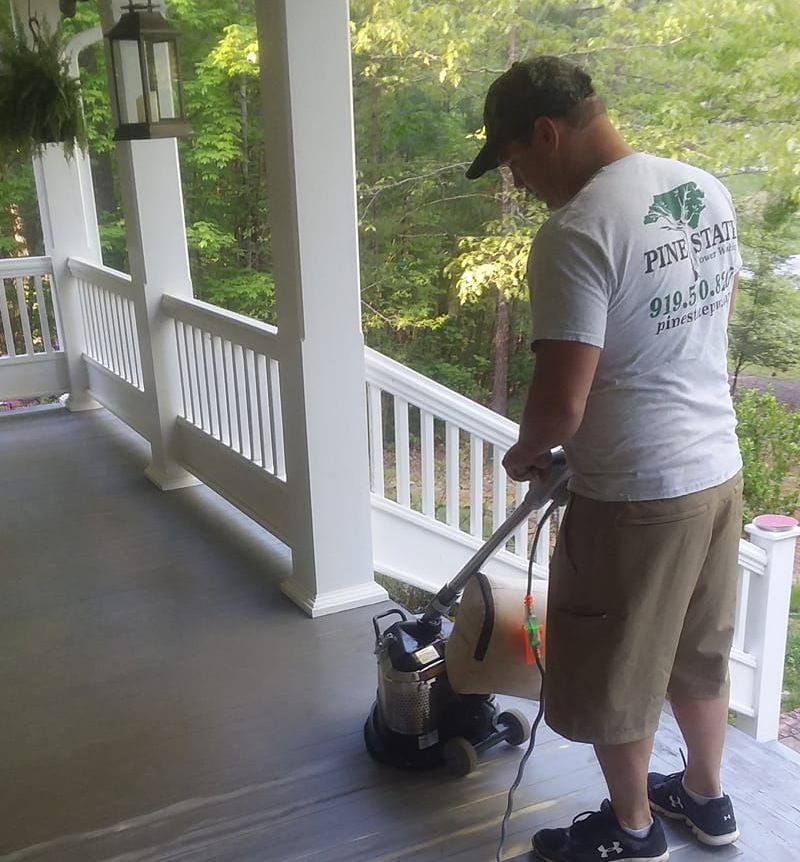 A man wearing a pine star shirt is using a vacuum cleaner on a porch