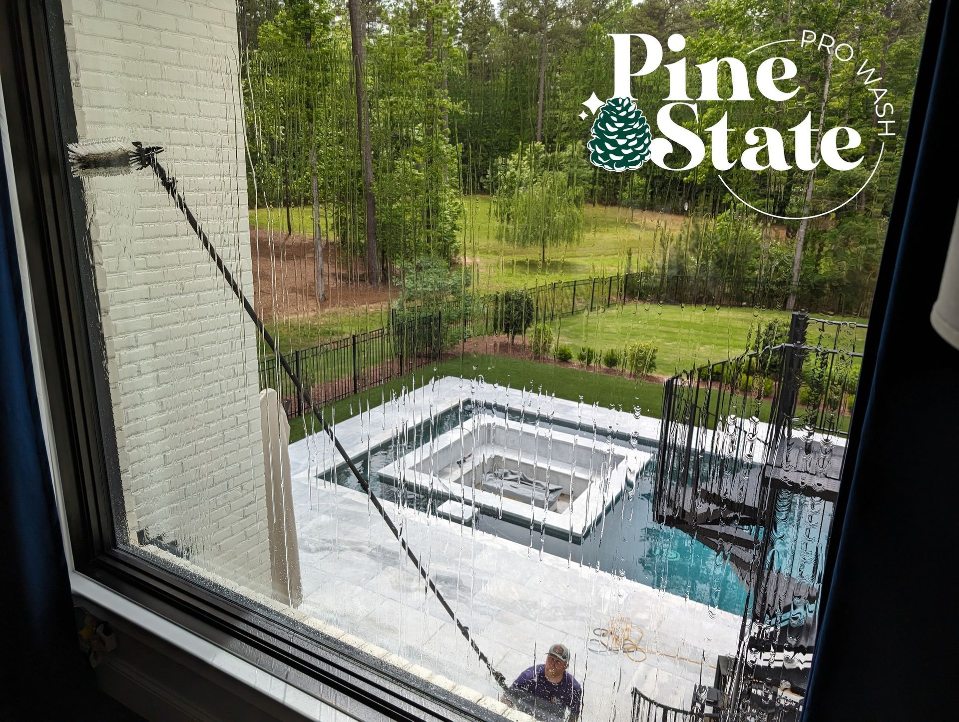 A man is cleaning a window of a house with a pool in the background.