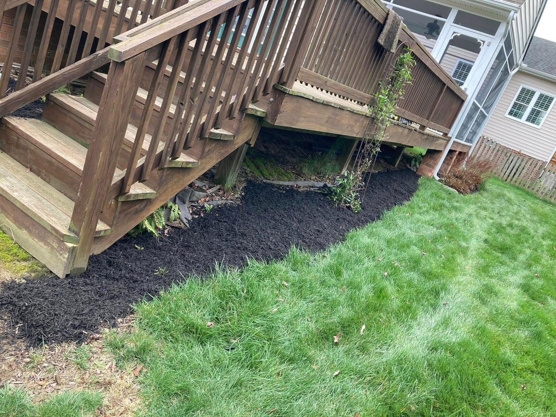 Wooden deck with steps, over a strip of black mulch bordering green grass.