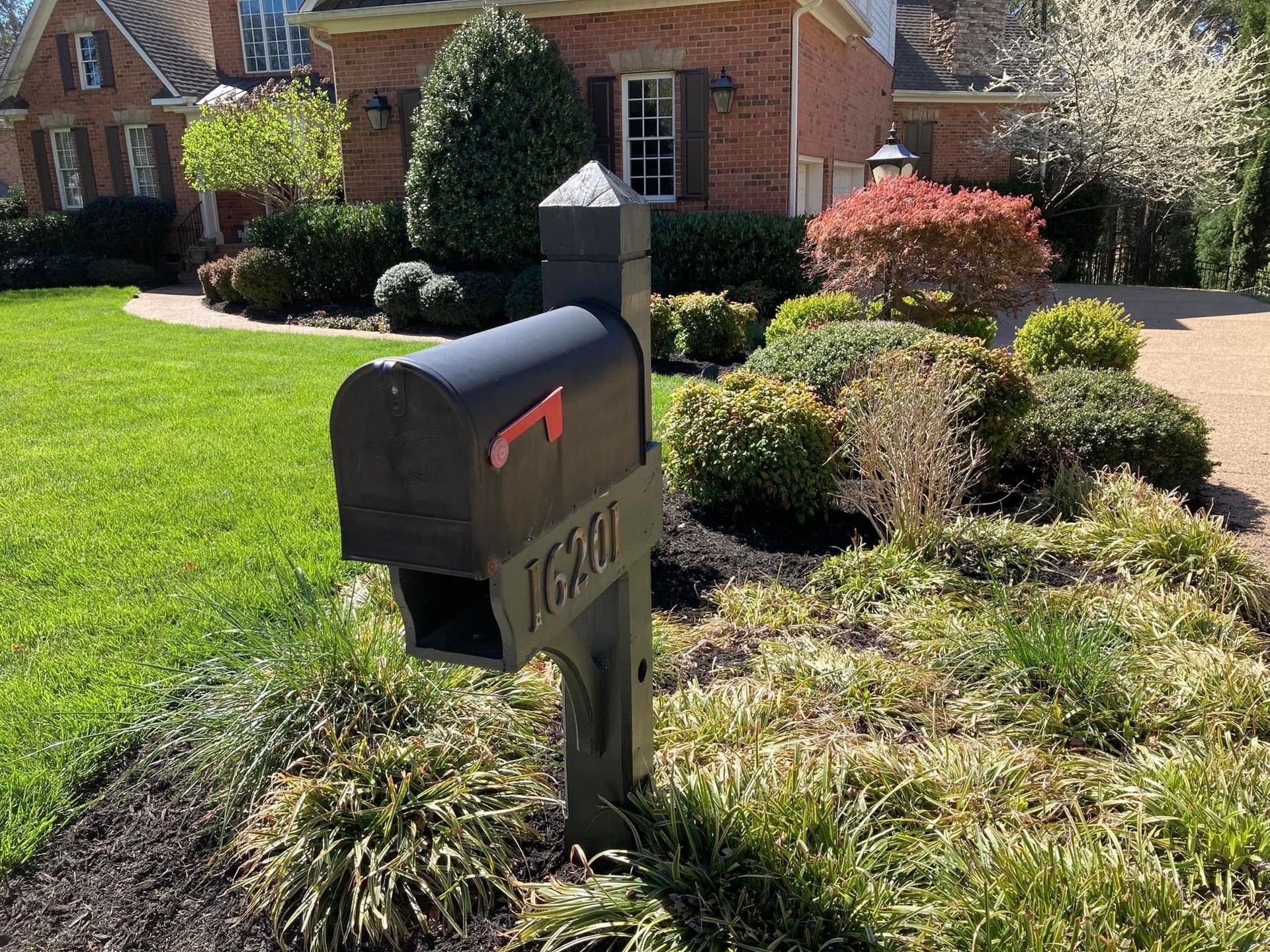 Black mailbox with address, in front yard of brick house with landscaping.