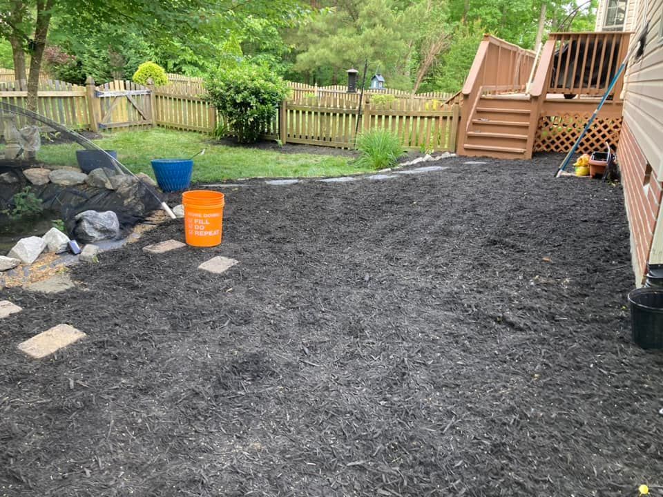 Backyard with fresh black mulch, a wooden deck, and a fence. An orange bucket is on the ground.