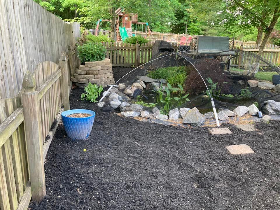 Backyard with a rock garden, sprinklers, and a blue planter near a wooden fence.