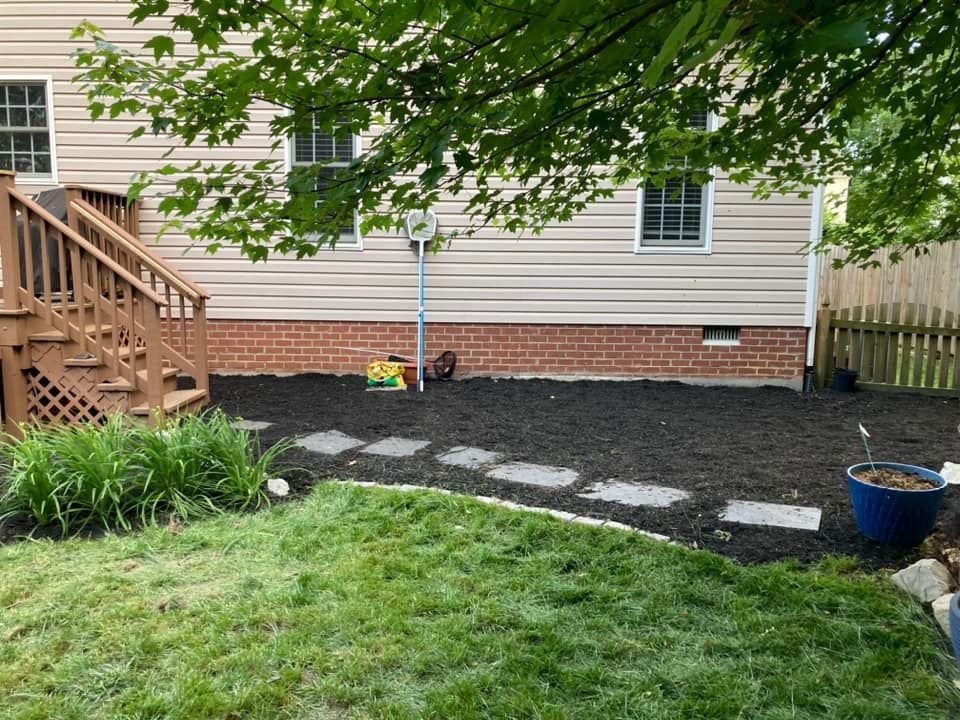 Backyard with fresh mulch, stepping stones, grass, deck, and house.