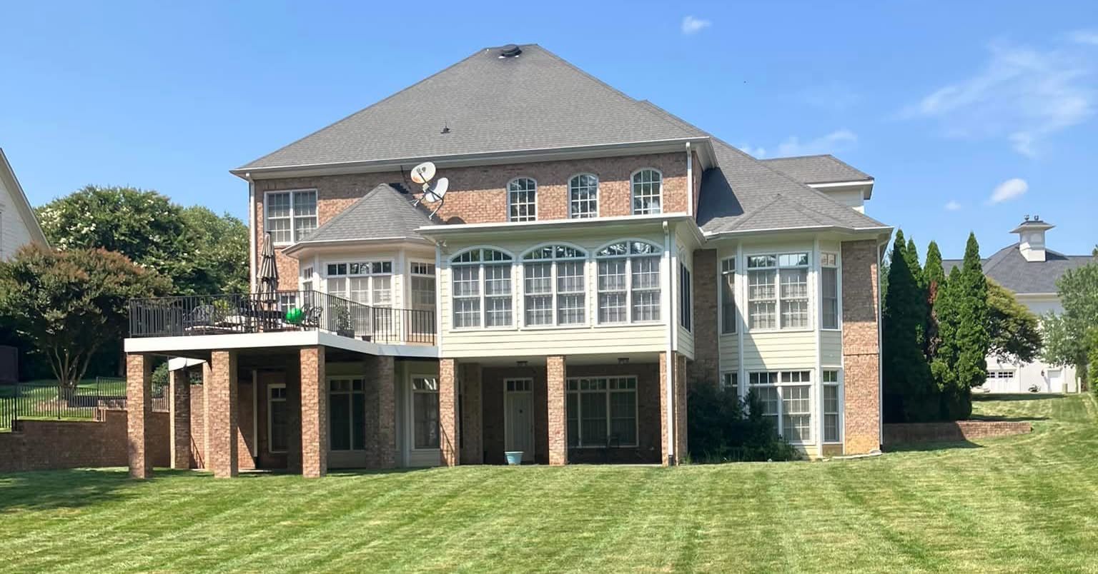 Rear view of a two-story brick house with a deck and large windows, set on a green lawn.