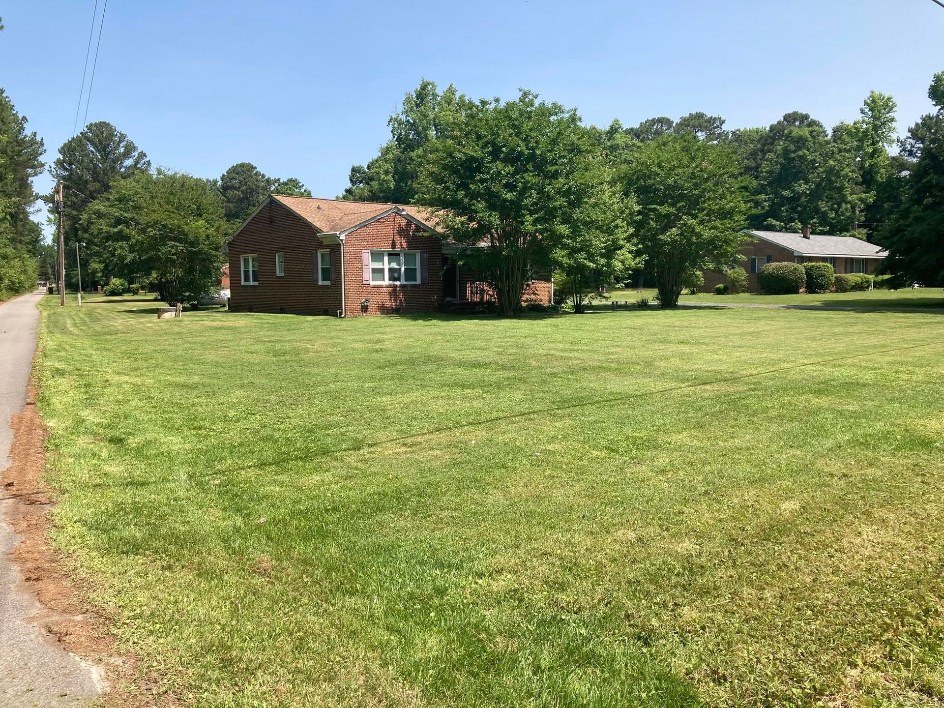Brick house with green lawn, trees, and blue sky.