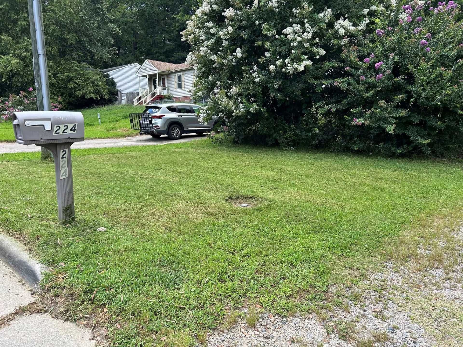 A mailbox on a post with the number 224, in front of a house and car on a grassy lawn.