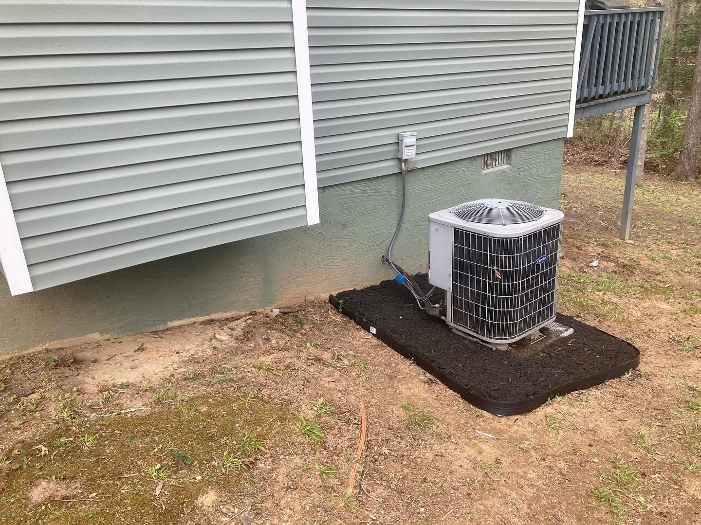 Air conditioner unit on a dark pad next to a house with gray siding.