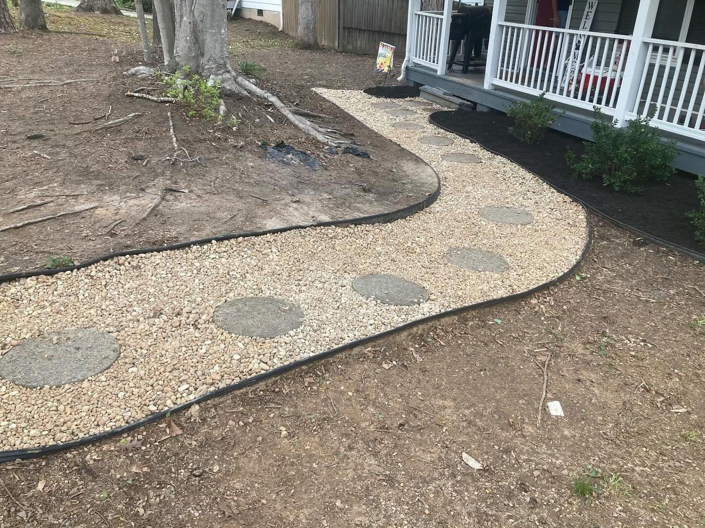A gravel path with stepping stones leads to a porch with white railing.