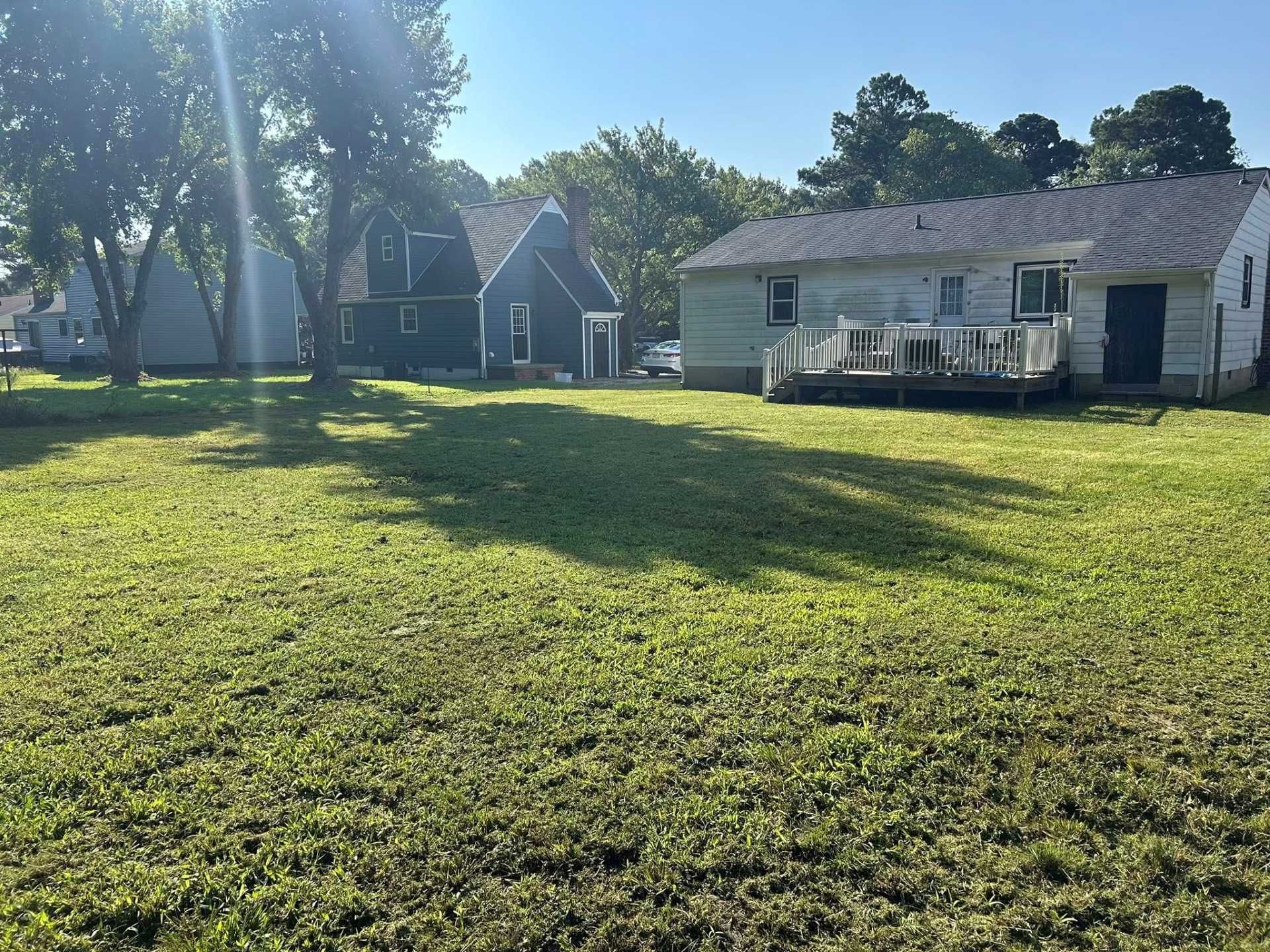 Grassy yard with two houses; one blue, one white. Sunlight and shadows cover the grass.