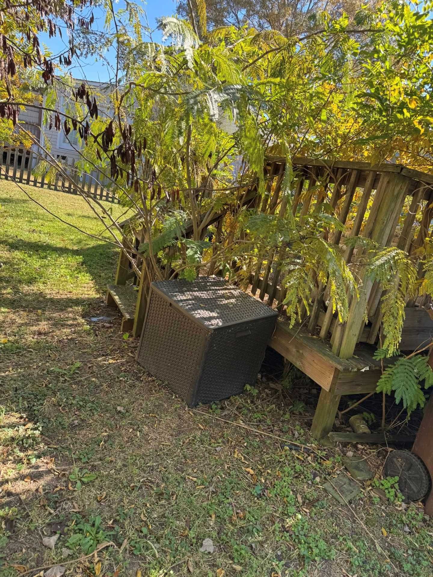 Brown wooden bench and square planter in a yard with sparse foliage.