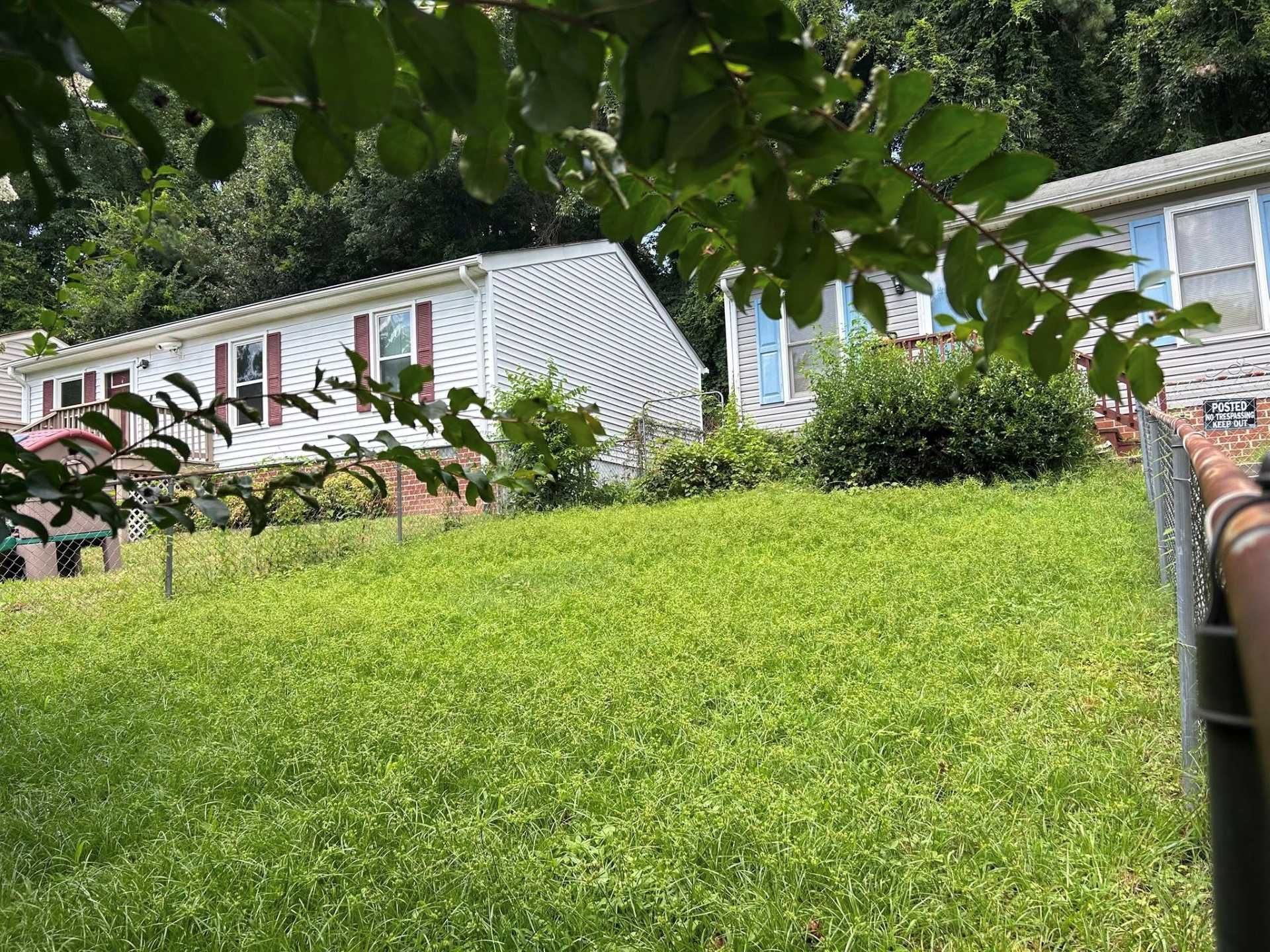 Row houses on a grassy hill; foliage in the foreground. White and blue siding, red shutters, and a chain link fence.