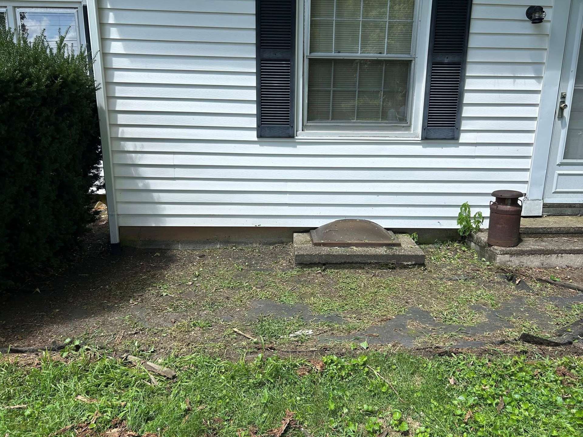 A white house exterior with a small, concrete access panel in a grassy area.
