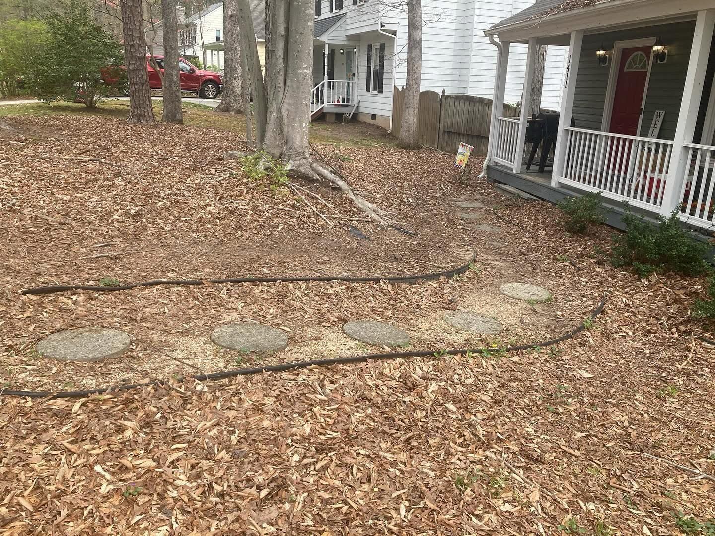 Yard covered in brown leaves, with a stone path leading to a white-columned porch with a red door.