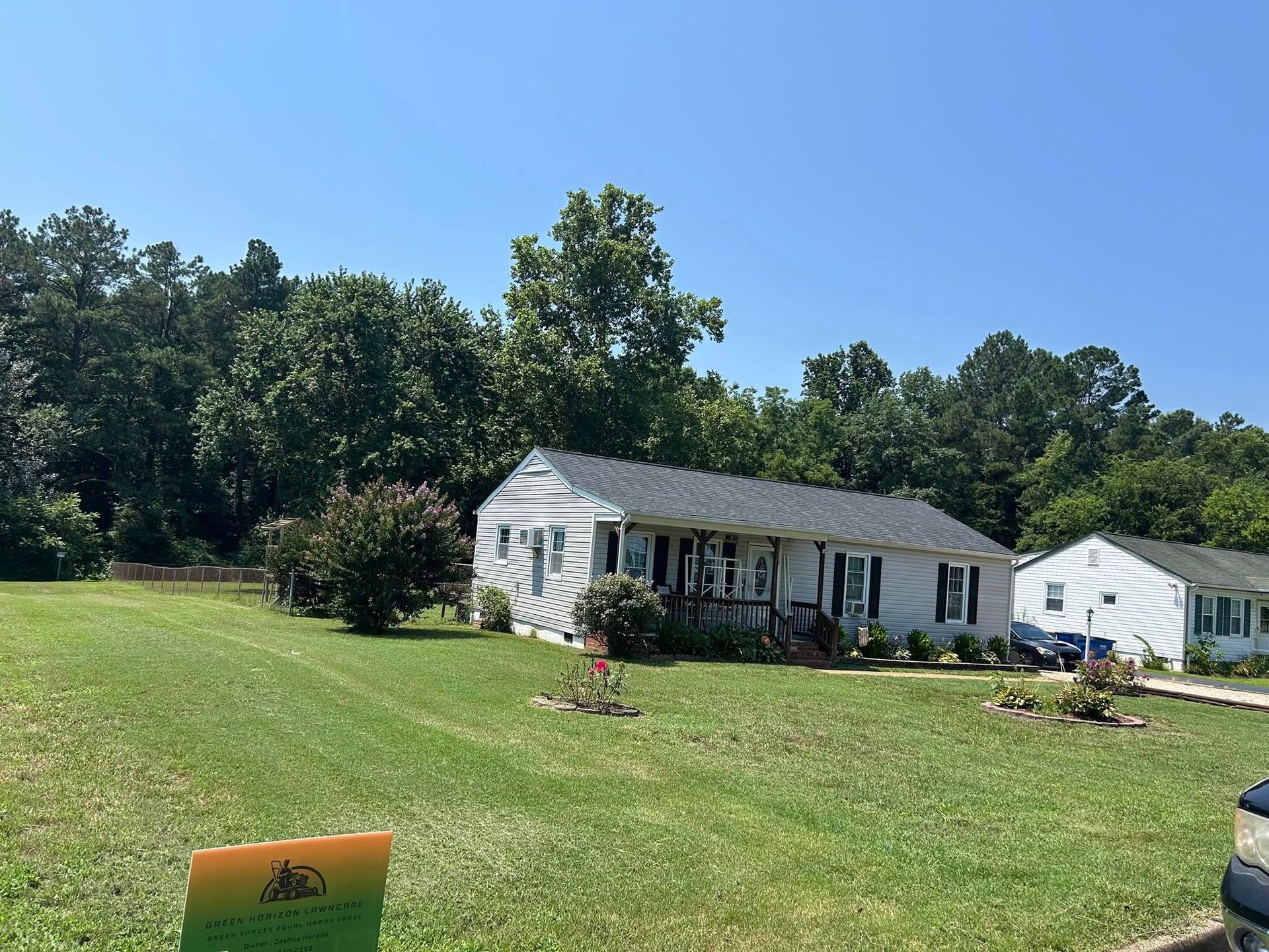 White bungalow with dark roof, lawn, and trees on a sunny day.