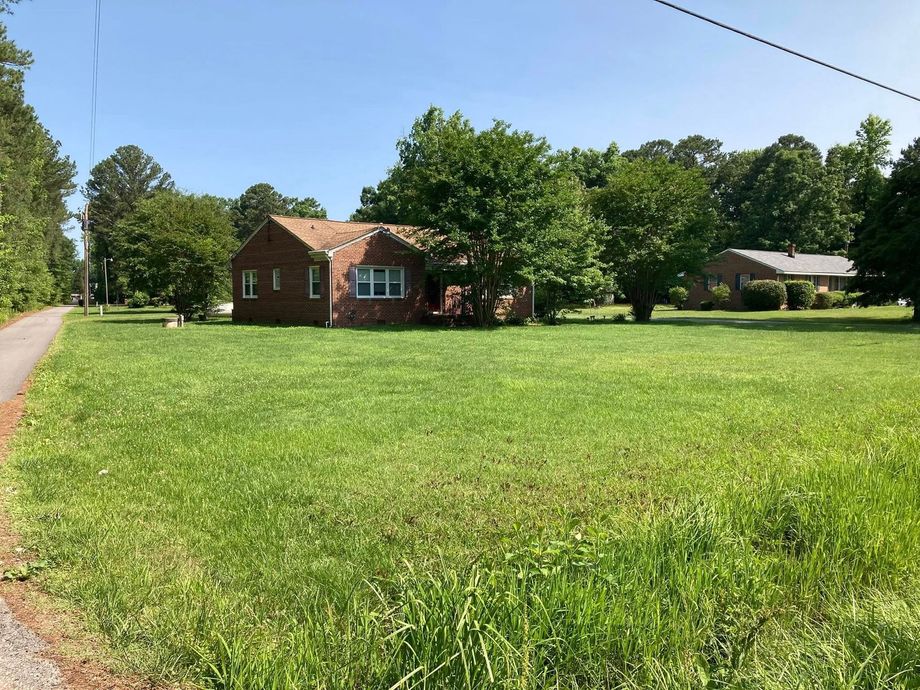 Brick house with a brown roof and a large, grassy yard on a sunny day.