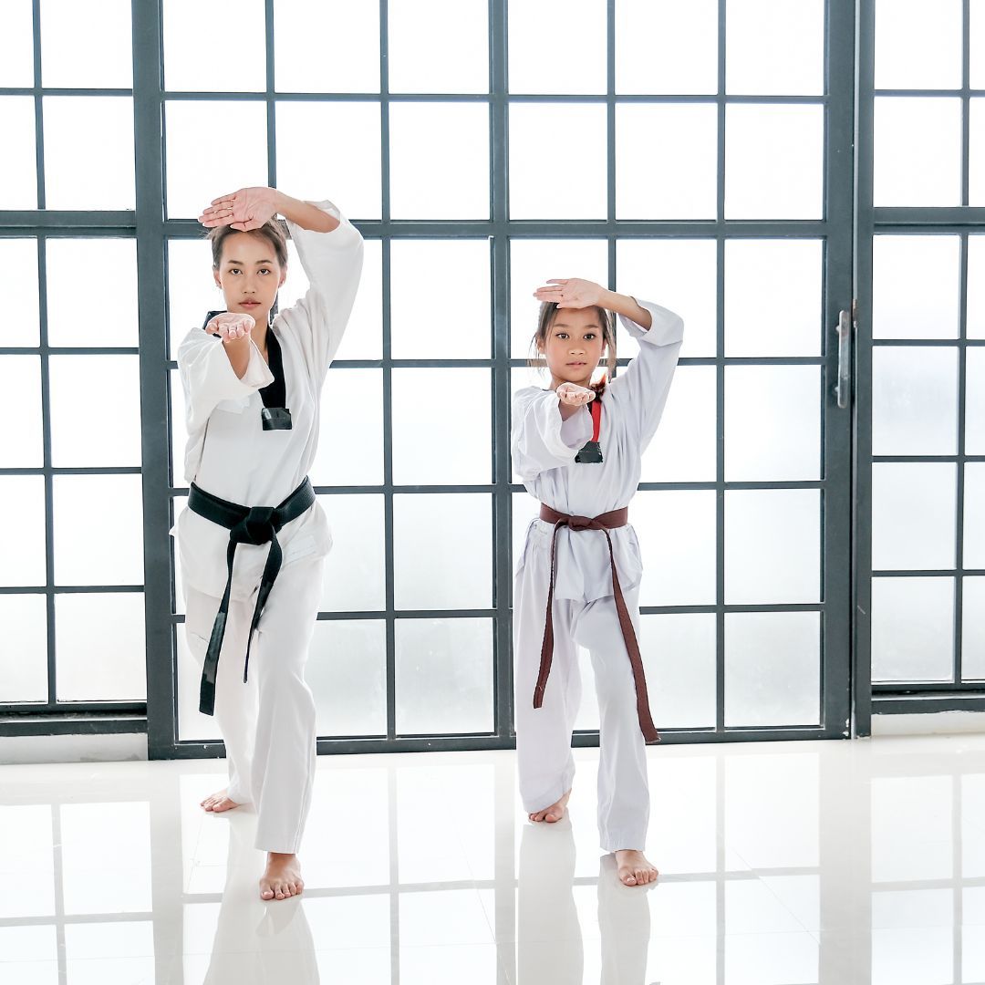 A young girl in a karate uniform is sitting on the floor.