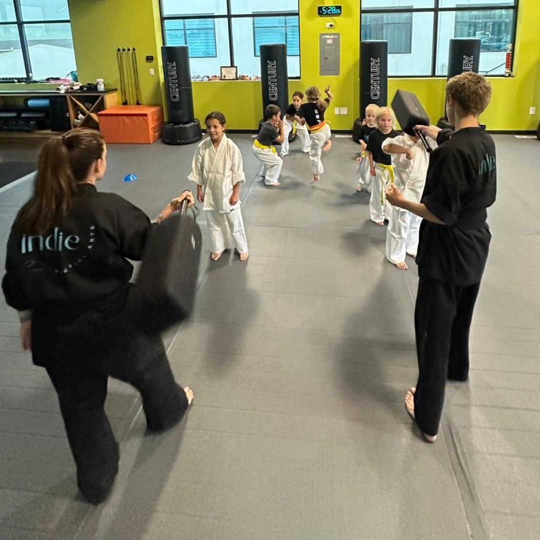 A young girl in a karate uniform is sitting on the floor.