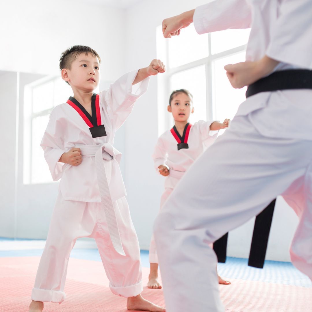 A group of children are practicing karate with a teacher in a gym.