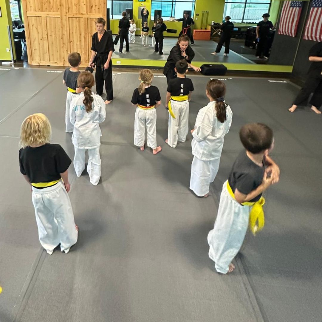 A group of children are practicing karate with a teacher in a gym.