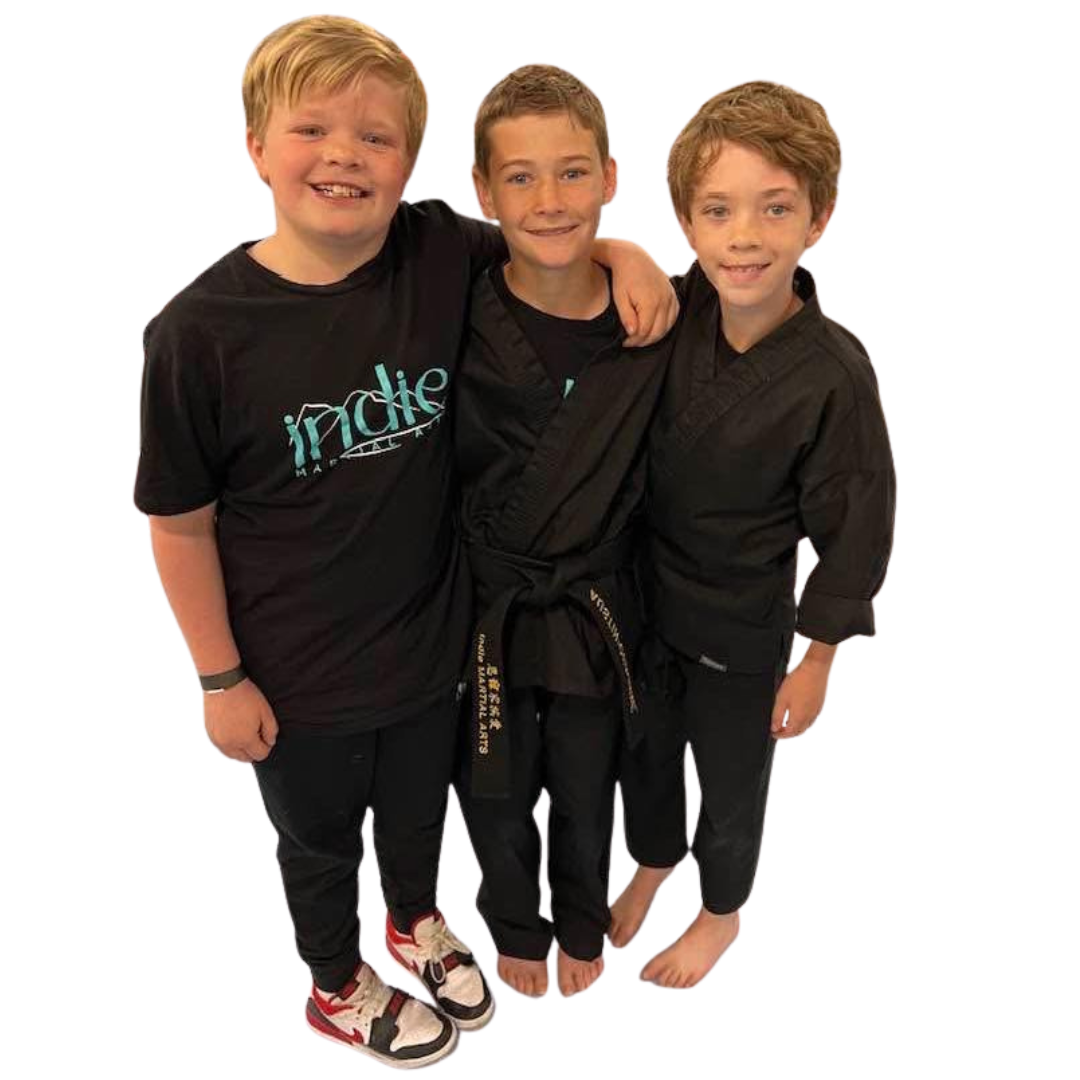 A boy and two girls are wearing karate uniforms and pointing at the camera