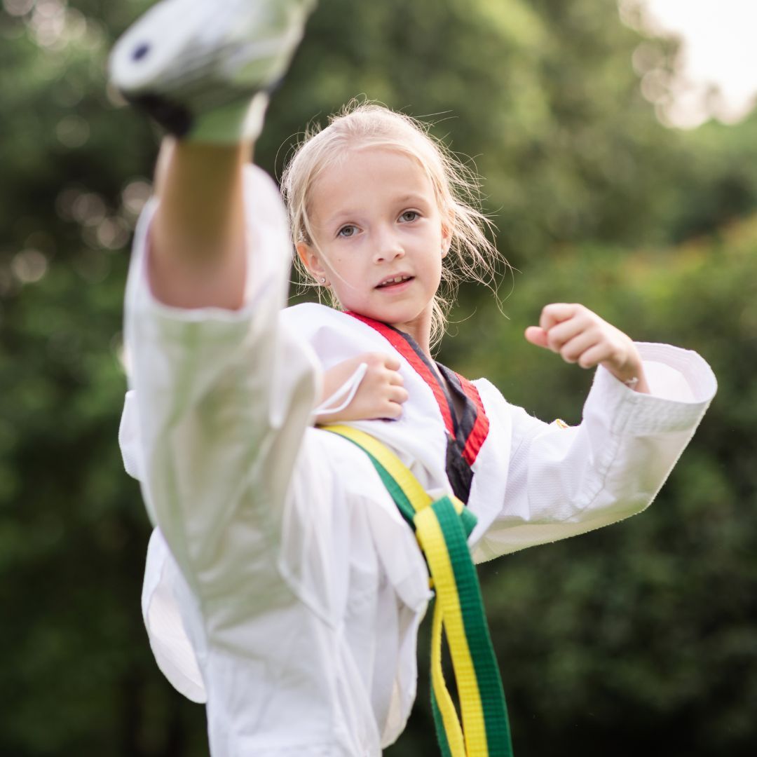 A man is kneeling down next to a young boy in a taekwondo class.