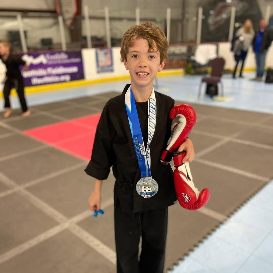 A man is kneeling down next to a young boy in a taekwondo class.