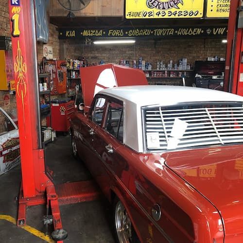 A Red Car With the Hood Up is on a Lift in a Garage — Coastal Automotive Services Long Jetty in Long Jetty, NSW