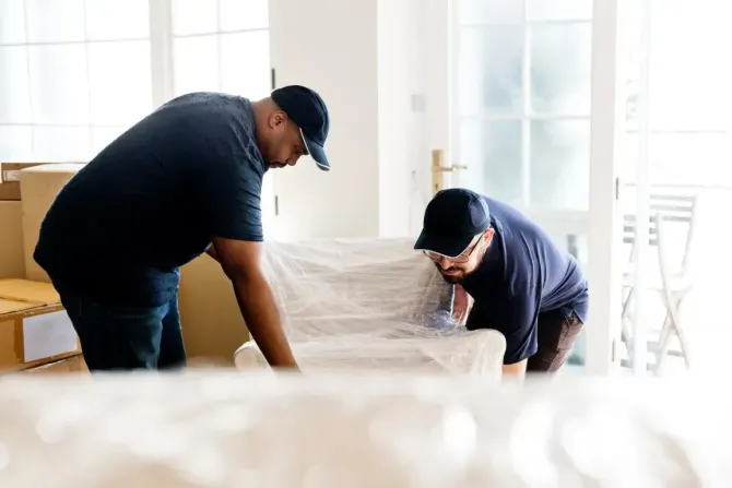 Two movers wrapping a couch in protective film.