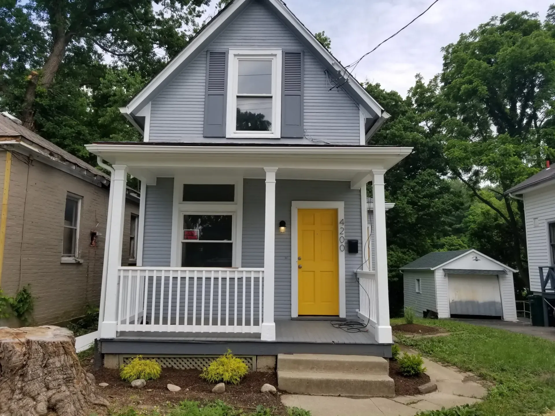 A small gray house with a yellow door and porch.