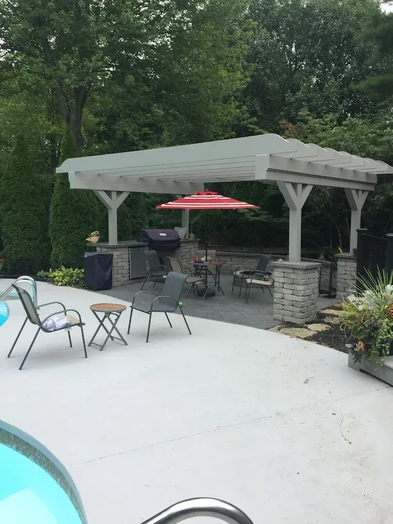 A patio with a pergola , chairs , tables and umbrellas next to a pool.