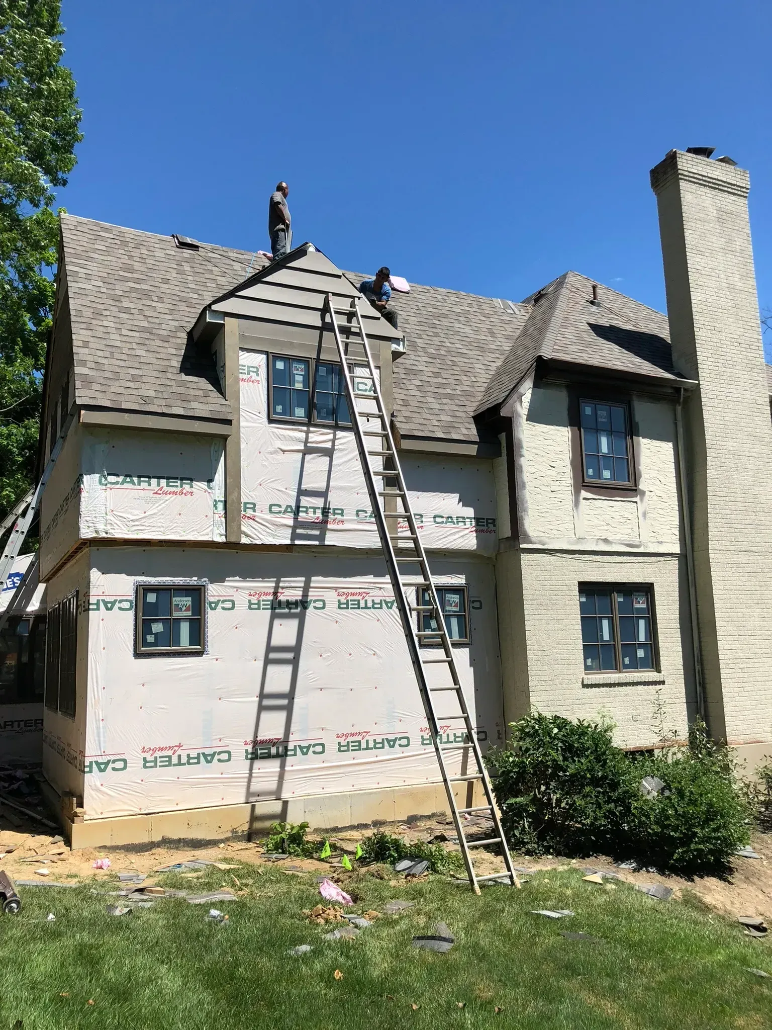 A man on a ladder is working on the roof of a house.