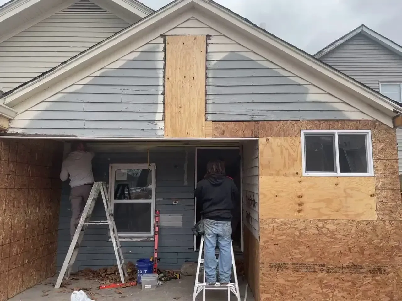 A couple of people standing on a ladder in front of a house.