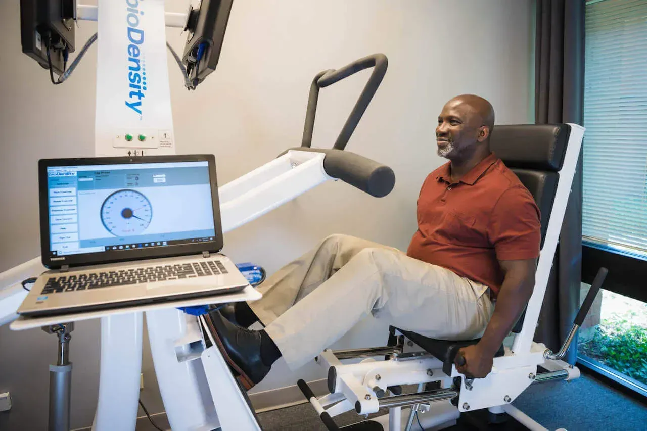 A man is sitting in a chair with his legs crossed in front of a laptop.
