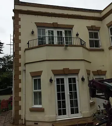 A large white house with a balcony and a crane in front of it.